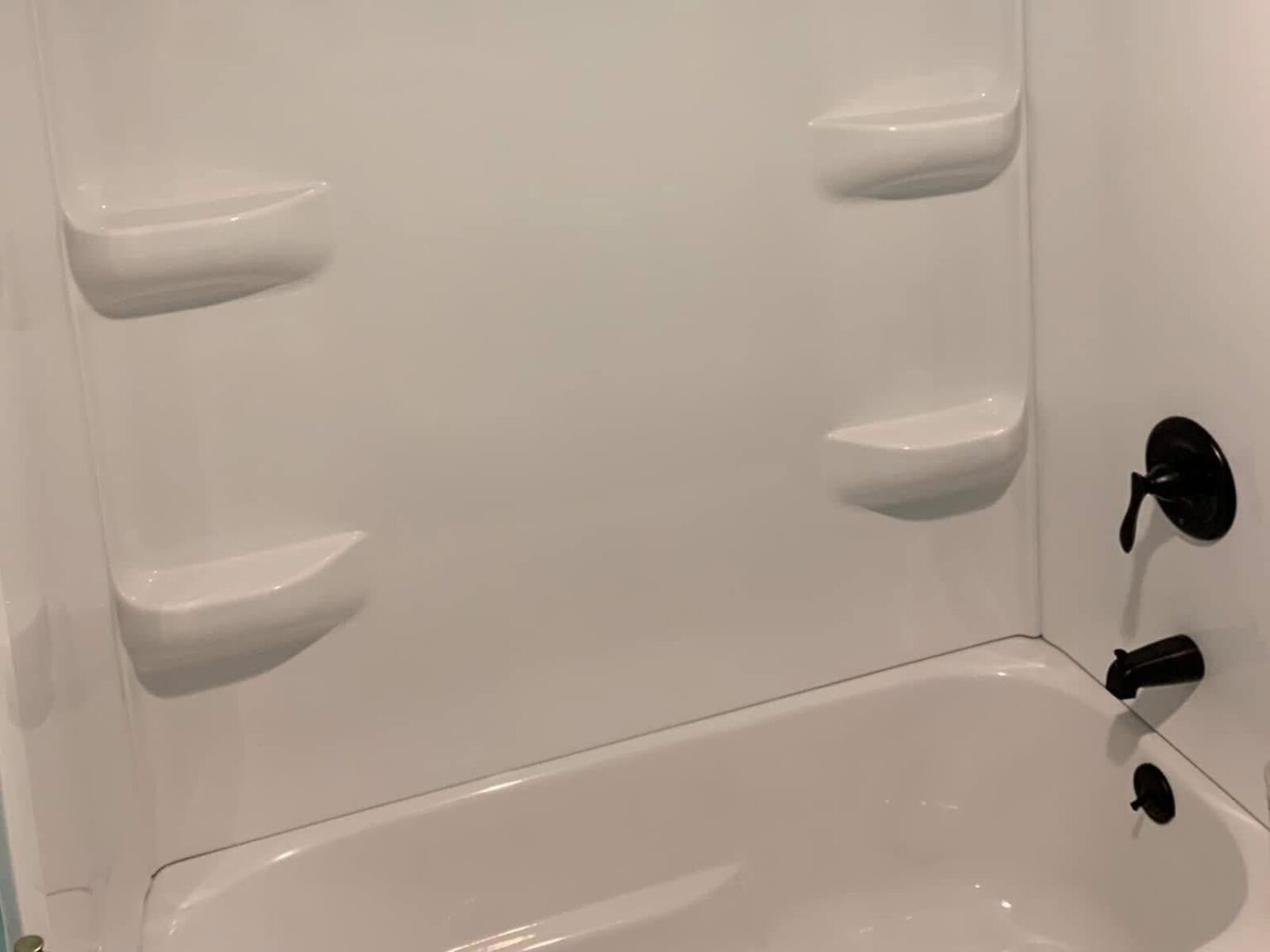 Finished bathtub with a new white shower surround, built-in shelves and bronze fixtures